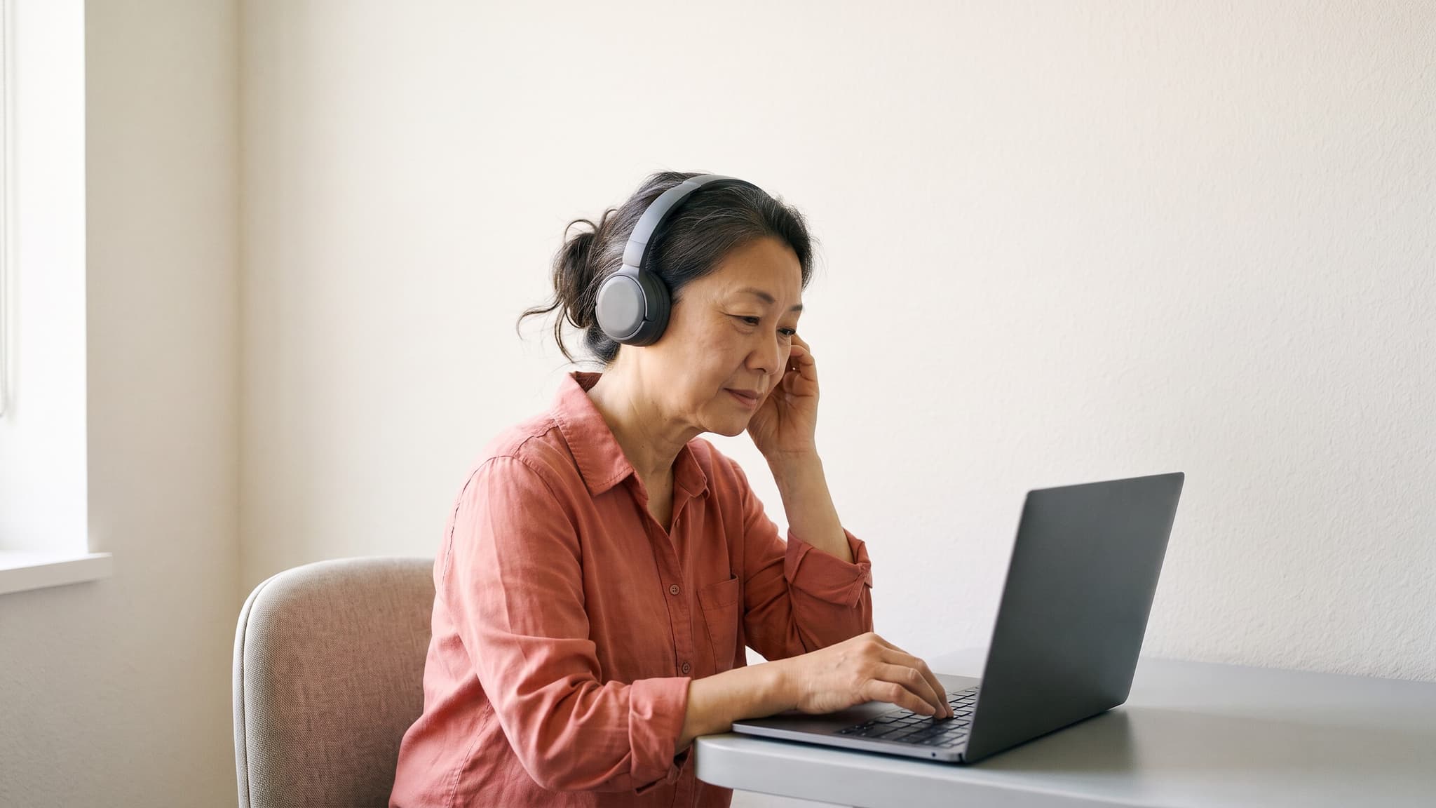A practitioner listens through headphones while carefully checking a consultation summary at her laptop.