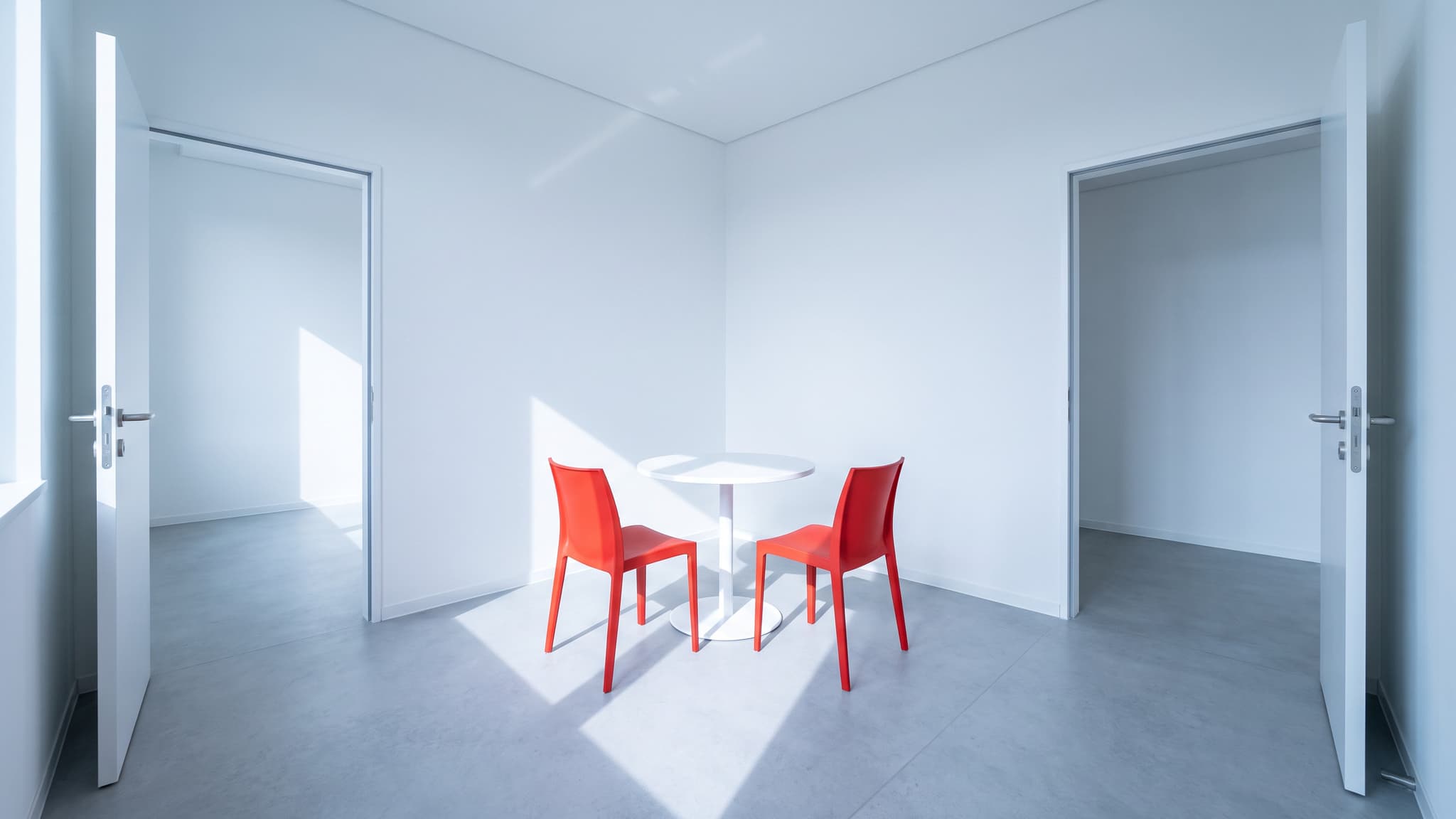 Two open doorways lead into one shared consultation space with a white table and two red chairs.