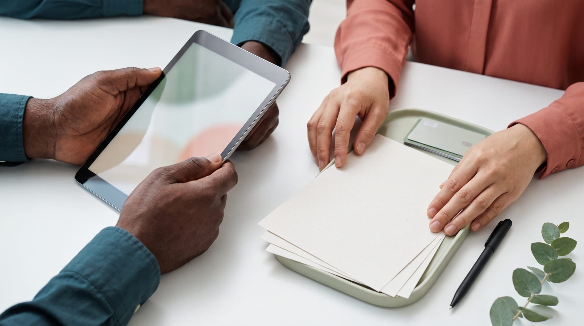 Hands reviewing a tablet, blank invoices, and a payment card at a practice desk