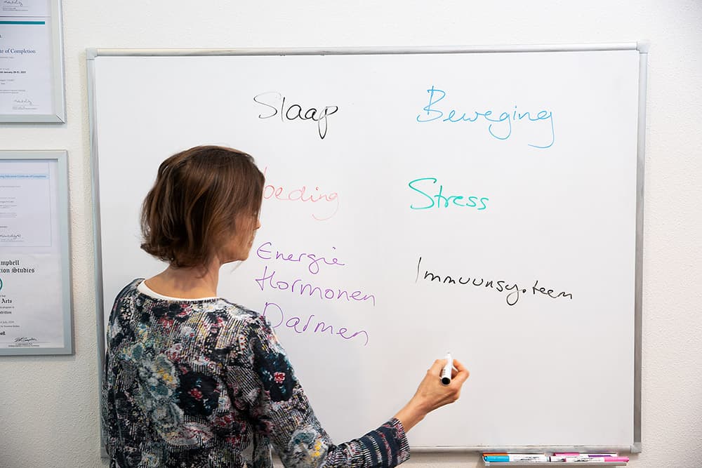 Practitioner at Newmedix writing sleep, food, movement and stress factors on the whiteboard